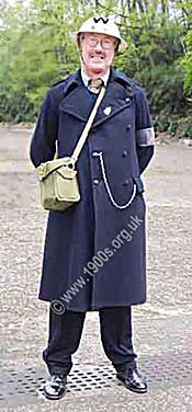 Man dressed in authentic 1940s ARP chief warden gear. Note the white helmet with its black W, the gas mask in its canvas bag, 
   the pocket chain carrying a whistle, the ARP armband and the ARP lapel badge