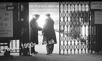 1940s ticket collector checking a passenger's train tickets as he enters a platform at a large city rail terminus