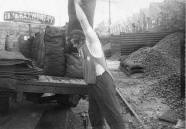 A coalman at a coal yard 
loading sacks of coal onto a delivery lorry, mid 20th century