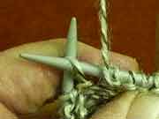 Detail of knitting a purl stitch, showing how the yarn is held in front of the knitting with right hand needle making the new stitch through the front of the old one.