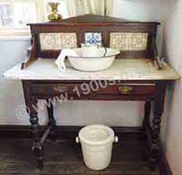 Old washstand, as used in Victorian and Edwardian Britain, with the customary marble top and the matching jug and bowl set. In this photo the jug and bowl set are made of enamel which would have been cheaper than decorated china.